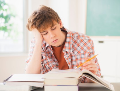 Teenage boy (14-15) sitting in classroom with pencil and books