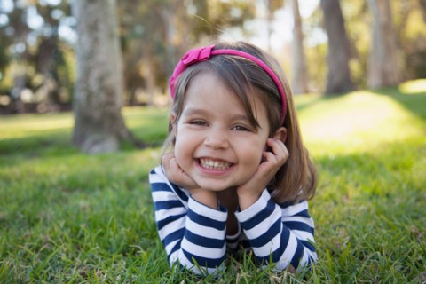 Portrait of smiling girl (4-5 years) lying on grass in park
