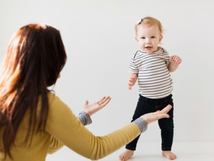 Mother raising hands towards her daughter (12-17 months)