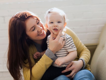 Portrait of mother sitting on sofa and touching face of her daughter's (12-17 months)