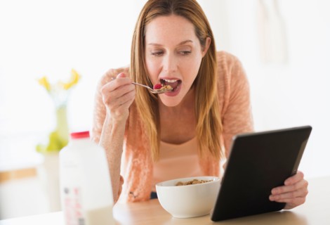 Woman eating breakfast and looking at tablet pc.