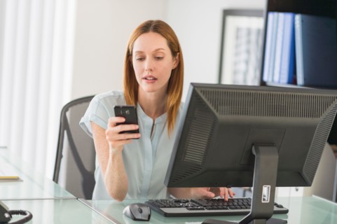 Business woman using computer and phone in office.