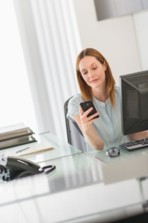 Business woman using computer and phone in office.