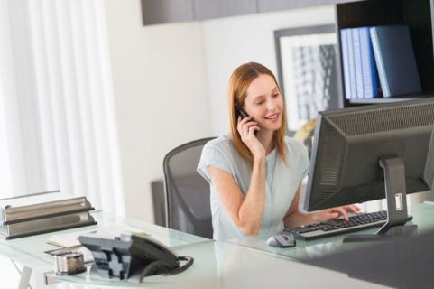 Business woman using computer and phone in office.