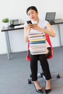 Businesswoman with stack of files texting on phone.