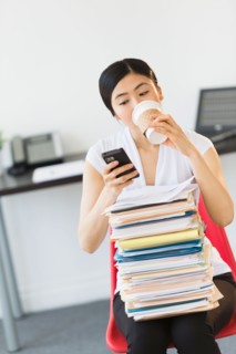 Businesswoman with stack of files texting on phone.