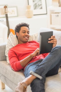 Man lying on sofa and using tablet PC.