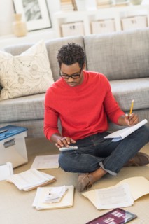 Man sitting on floor in living room and calculating bills.