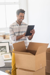 Man using tablet PC while unpacking cardboard box.