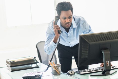 Businessman working on computer and talking on cell phone.