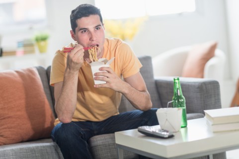 Man eating take out meal and watching television.