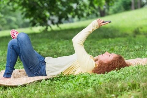 Woman lying on grass in park and using mobile phone.