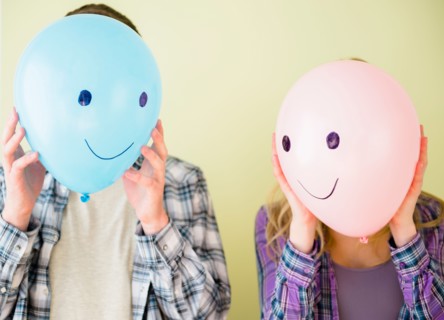 Studio shot of couple holding balloons with smiley faces in front of their heads