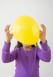 Studio shot of girl (8-9) hiding behind balloon