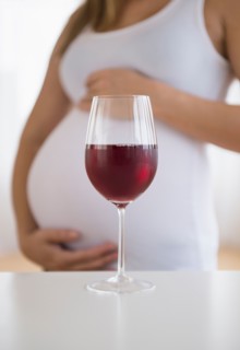 Mid section of pregnant woman, red wine in front