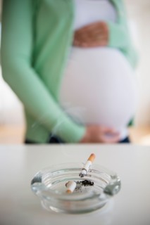Mid section of pregnant woman, ashtray and cigarette in front