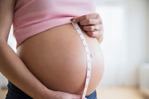 Mid section of pregnant woman measuring her belly
