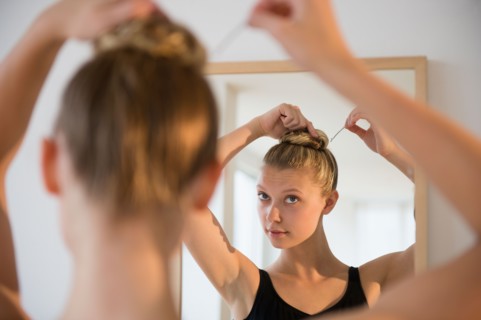 Rear view of teenage (16-17) ballerina looking into mirror and styling her hair