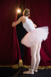 Teenage (16-17) ballerina on stage looking through curtain