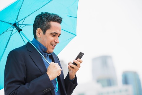 Portrait of man holding blue umbrella and using mobile phone