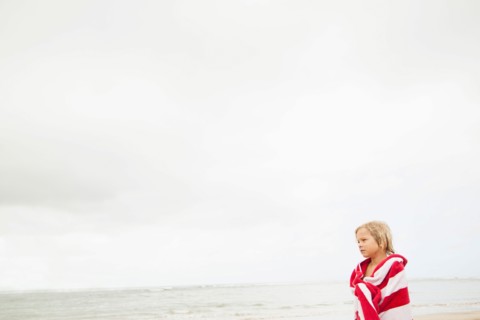 Boy (6-7) wrapped in towel on beach