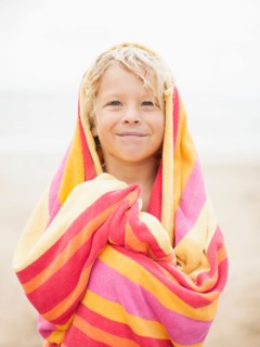 Boy (6-7) wrapped in towel on beach