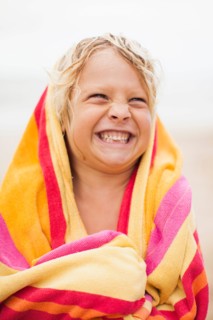 Boy (6-7) wrapped in towel on beach