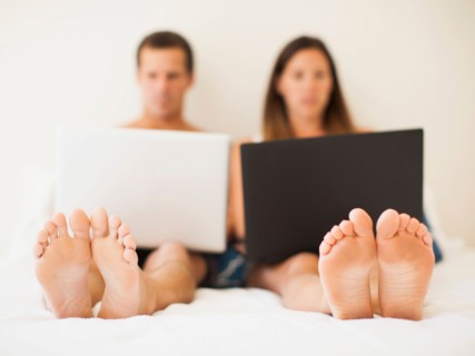 Couple lying on bed with laptops
