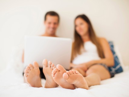 Couple lying on bed with laptop