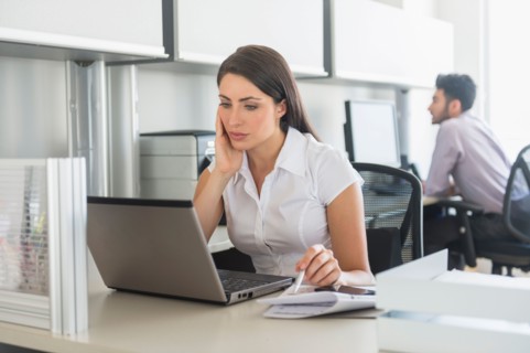 Woman working in office, man in background.