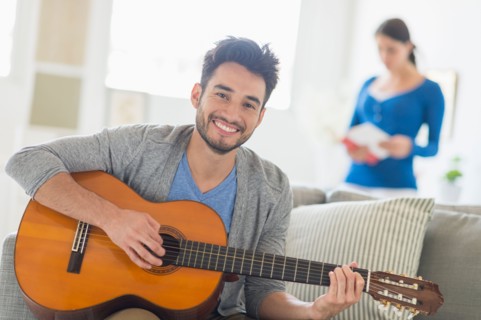 Man playing guitar, woman in background.