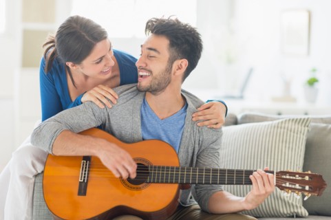 Man playing guitar while woman embracing him.