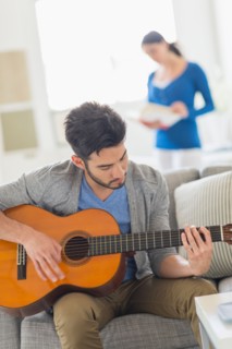 Man playing guitar, woman in background.