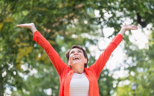 Happy mature woman raising hands in park.