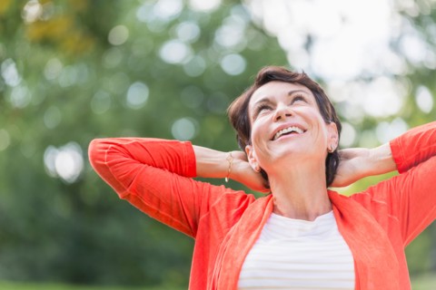 Happy mature woman raising hands in park.