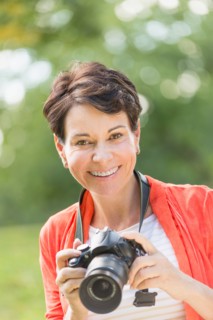 Mature woman holding camera in park.