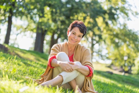 Mature woman sitting on grass in park.
