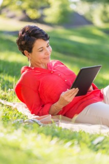 Mature woman lying on grass and using digital tablet.