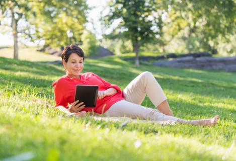 Mature woman lying on grass and using digital tablet.