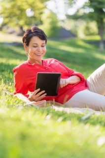 Mature woman lying on grass and using digital tablet.