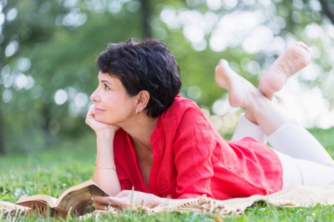Mature woman lying on grass and reading book.