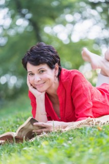 Mature woman lying on grass and reading book.