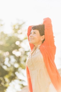 Mature woman raising hands in sunlight.