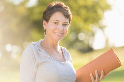 Mature woman holding yoga mat outdoors.