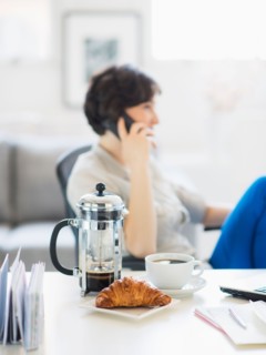 Woman talking on phone, coffee and croissant in foreground