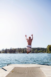 Young man jumping to lake from jetty