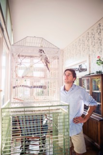 Portrait of young man standing by bird cage and looking at parrot