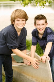 Two boys (12-13) posing with boat on grass near lake