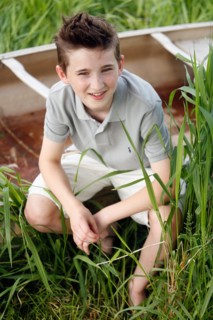 Boy (12-13) crouching on grass near boat