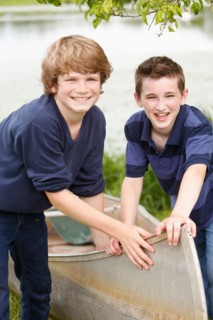 Two boys (12-13) posing with boat on grass near lake